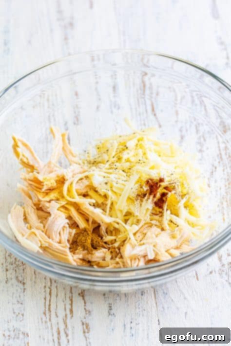 Date Night White Chicken Enchiladas 5 A glass bowl with chicken, half of the cheese, pepper, garlic powder, cumin, onion powder, salt, and chipotle powder.