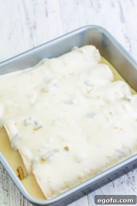 Date Night White Chicken Enchiladas 11 White sauce on top of chicken enchiladas in a baking dish.