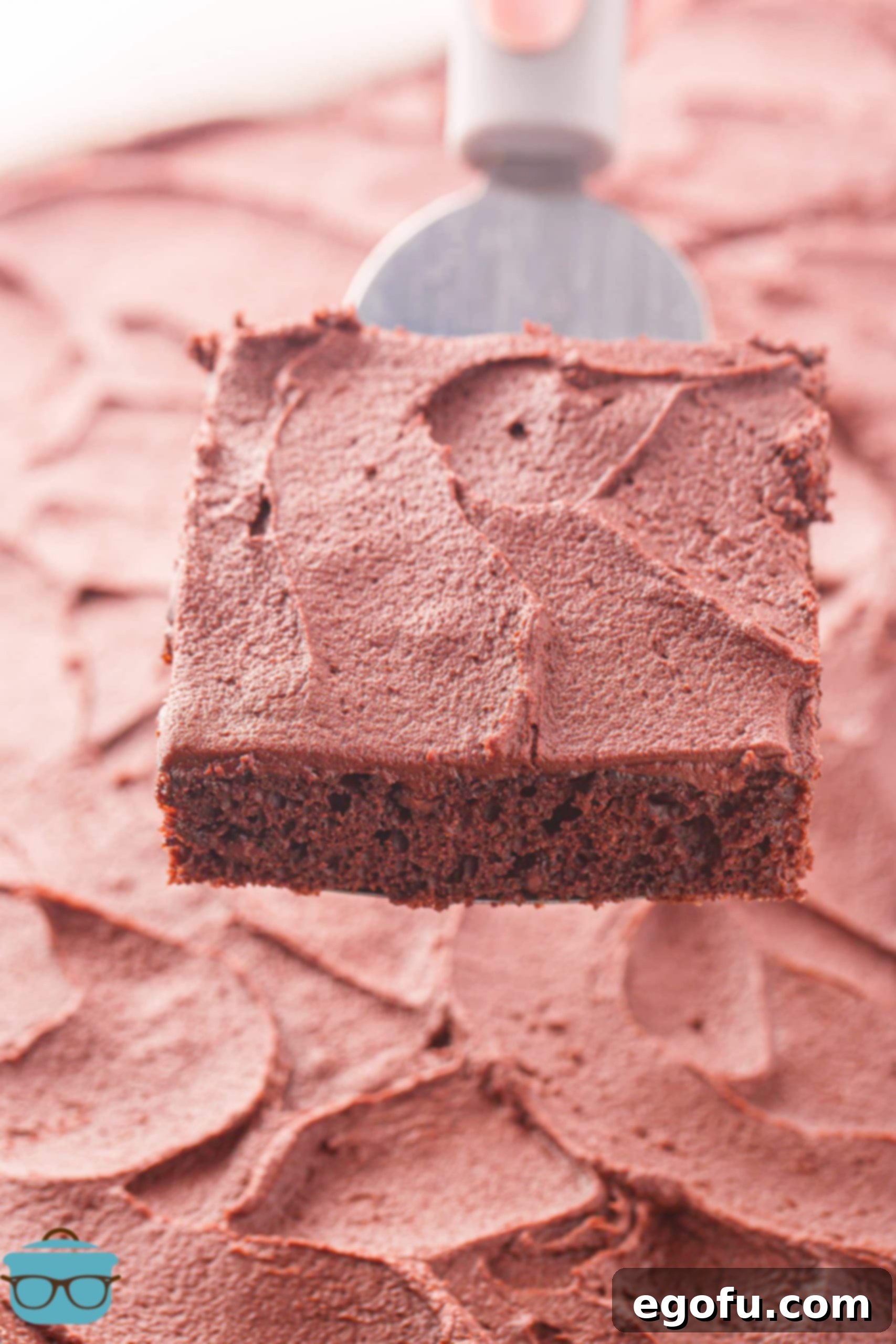A serving utensil holding a slice of Chocolate Sheet Cake, showcasing its moist interior and generous frosting.