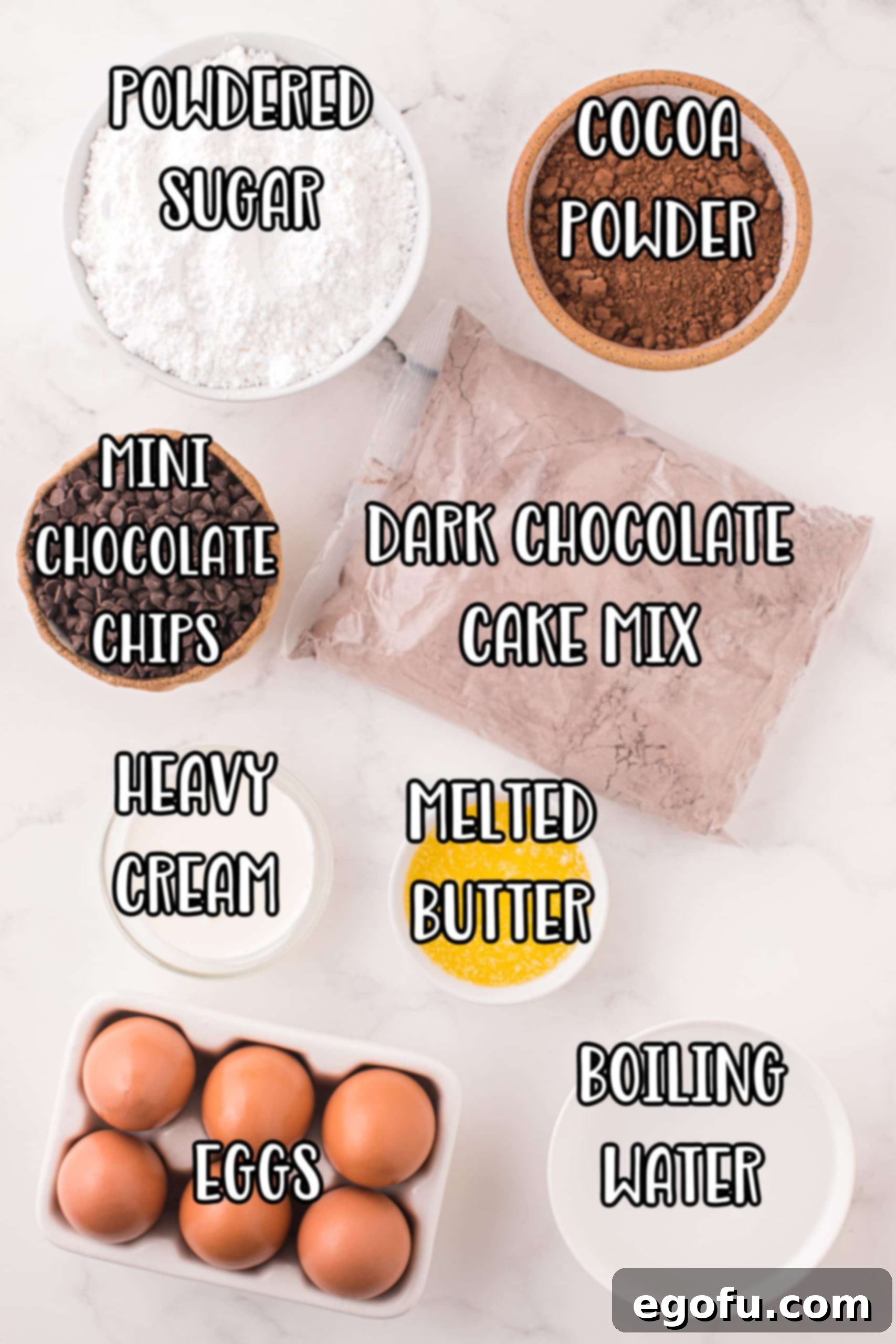 A flat lay of all the essential ingredients for making the Chocolate Sheet Cake: powdered sugar, chocolate cake mix, cocoa powder, mini chocolate chips, heavy cream, melted butter, water, and eggs.