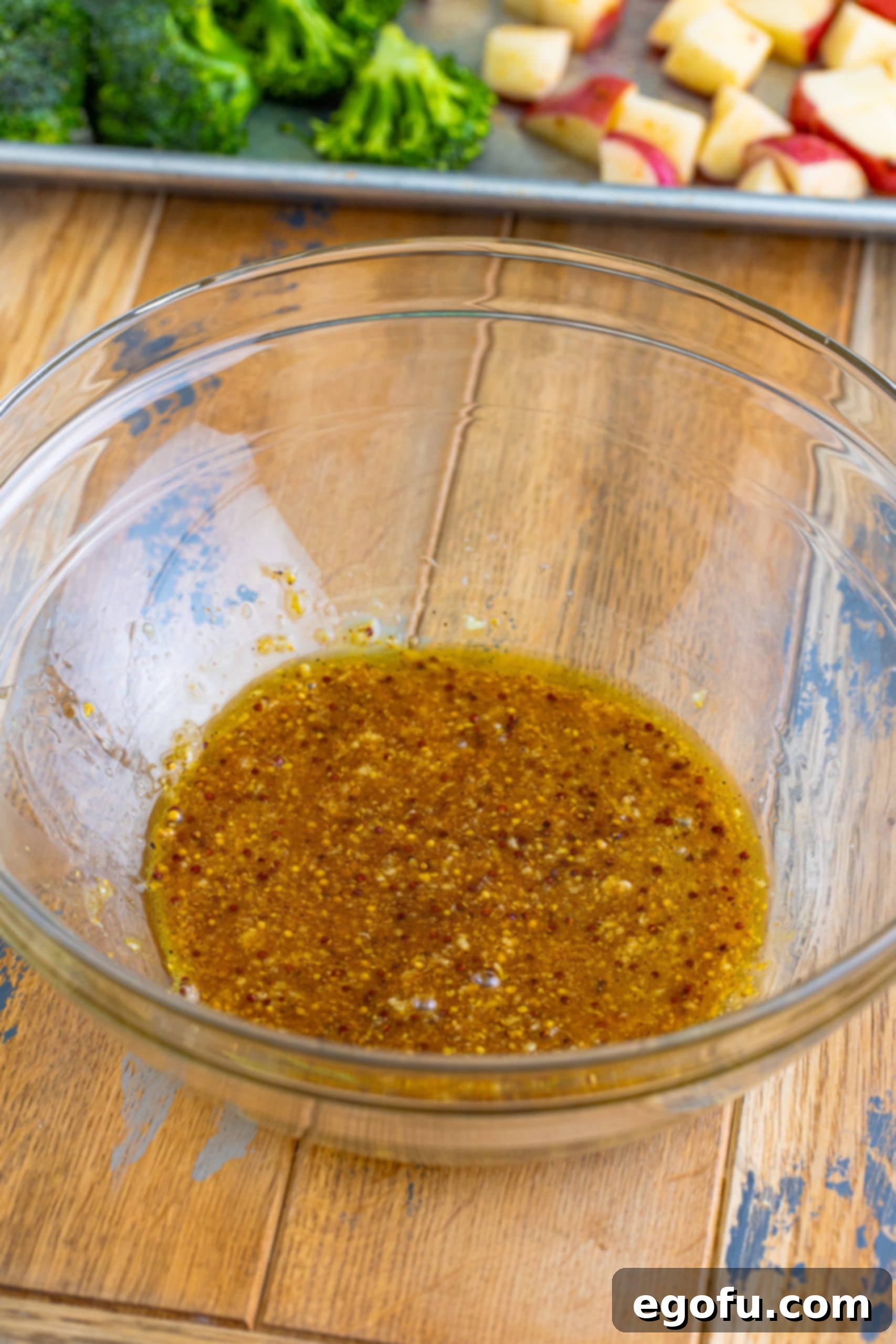 A glass bowl with honey, olive oil, mustard, garlic, and creole seasoning, whisked to form a glaze.