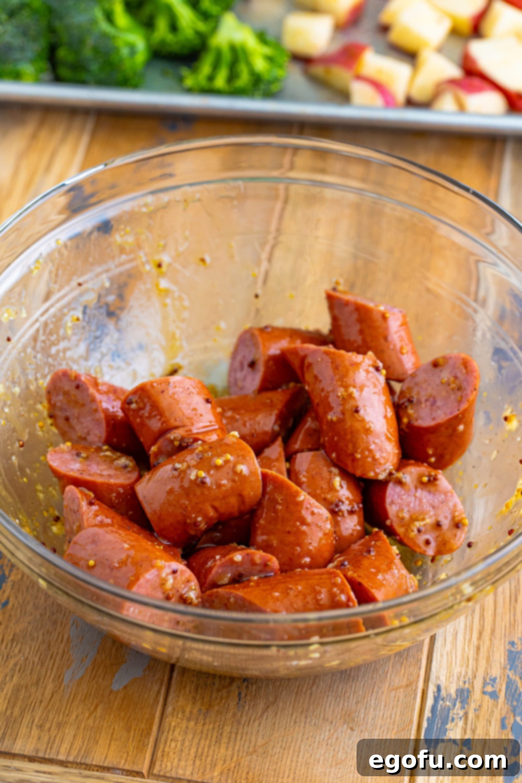 Kielbasa coated in sauce in a bowl, ready to join the vegetables.
