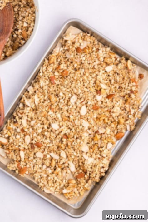 Spread out baked granola on a tray after stirring.