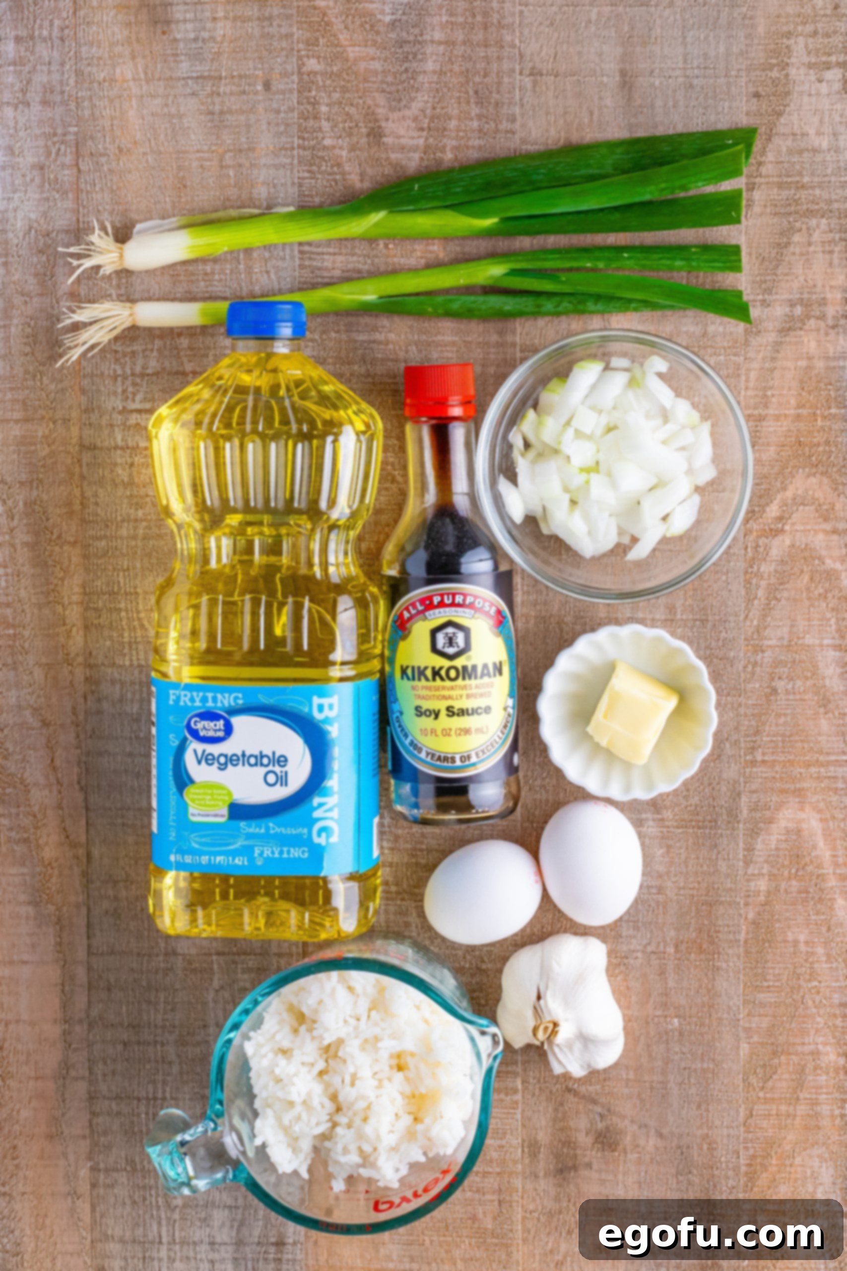 A vibrant flat lay of fresh ingredients: green onions, vegetable oil, beaten eggs, white rice, butter, soy sauce, and diced sweet onion, ready for cooking.