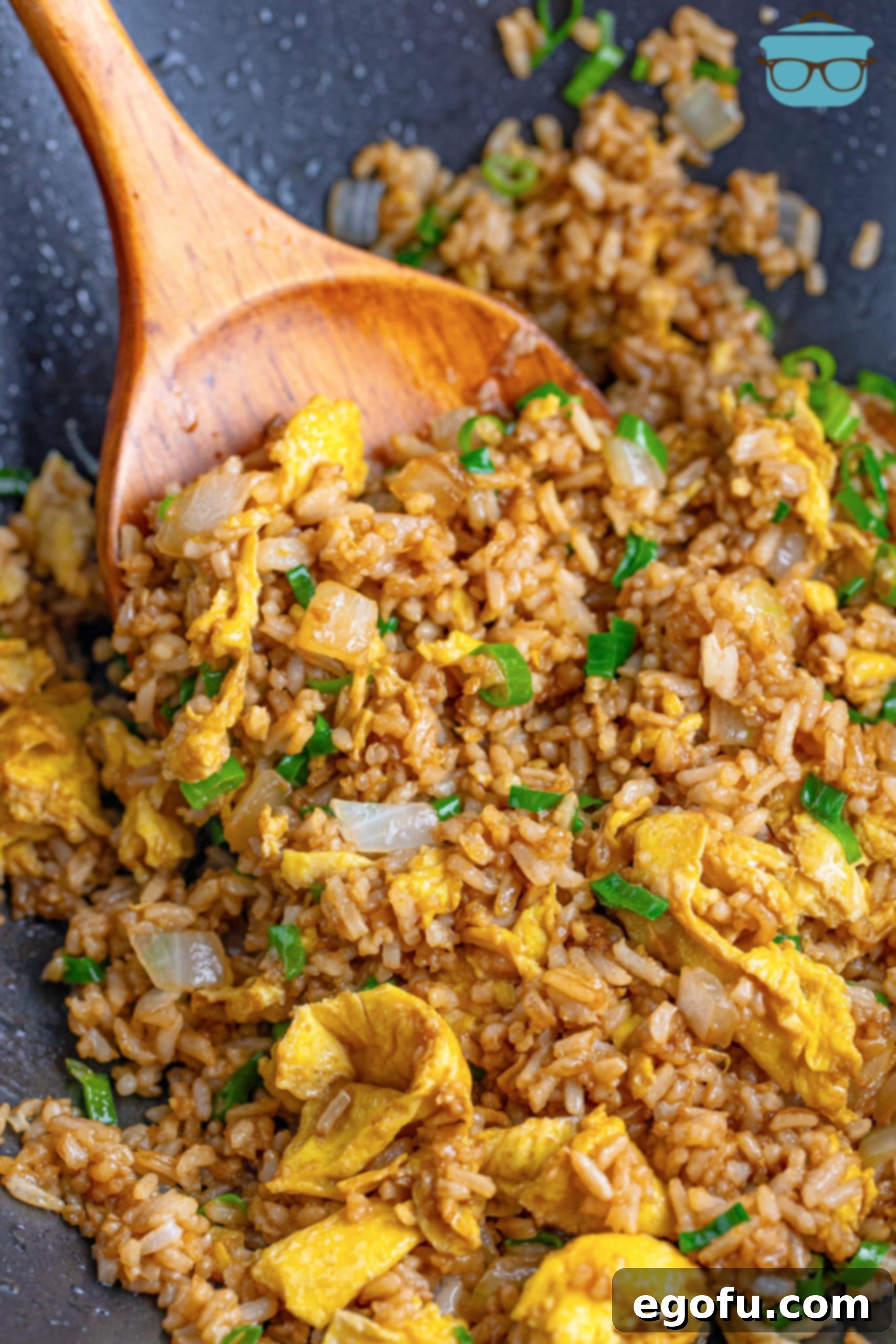 A wooden spoon scoops a generous portion of steaming, flavorful homemade Hibachi Fried Rice from the wok.