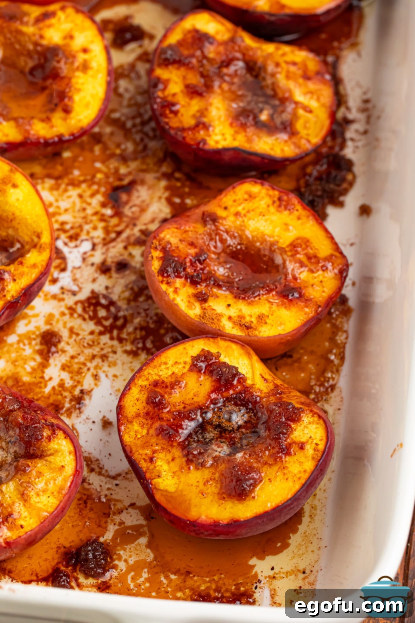 A few Baked Peaches in a baking dish, glistening with sauce and ready to be served.