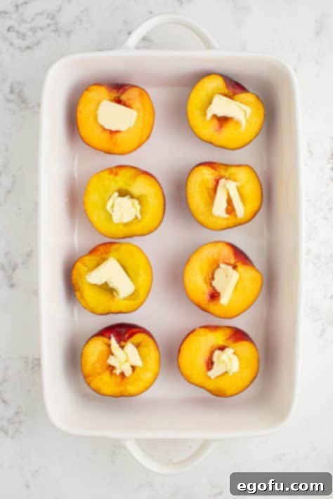 Peach halves in a baking dish, each with a piece of butter in its center.