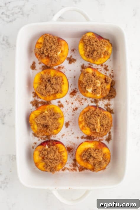 Brown sugar and cinnamon sprinkled over buttered peach halves in a baking dish.