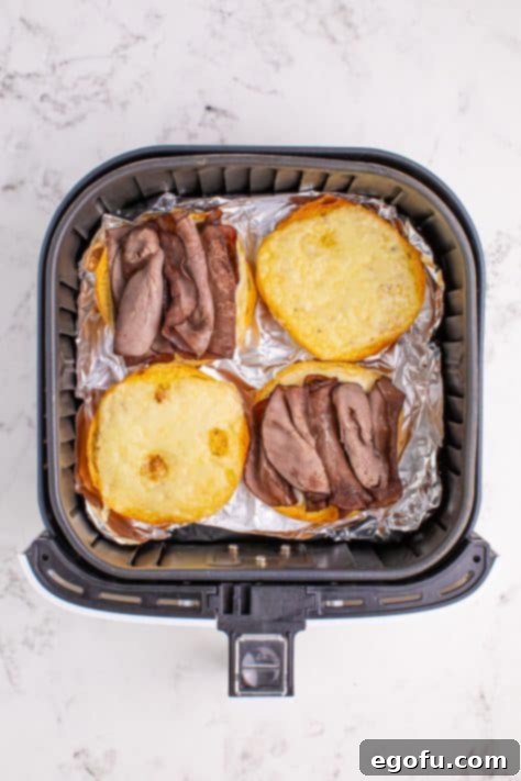 Ultimate Air Fryer Roast Beef Melts 12 Cheese and Beef sandwiches in an Air Fryer basket.
