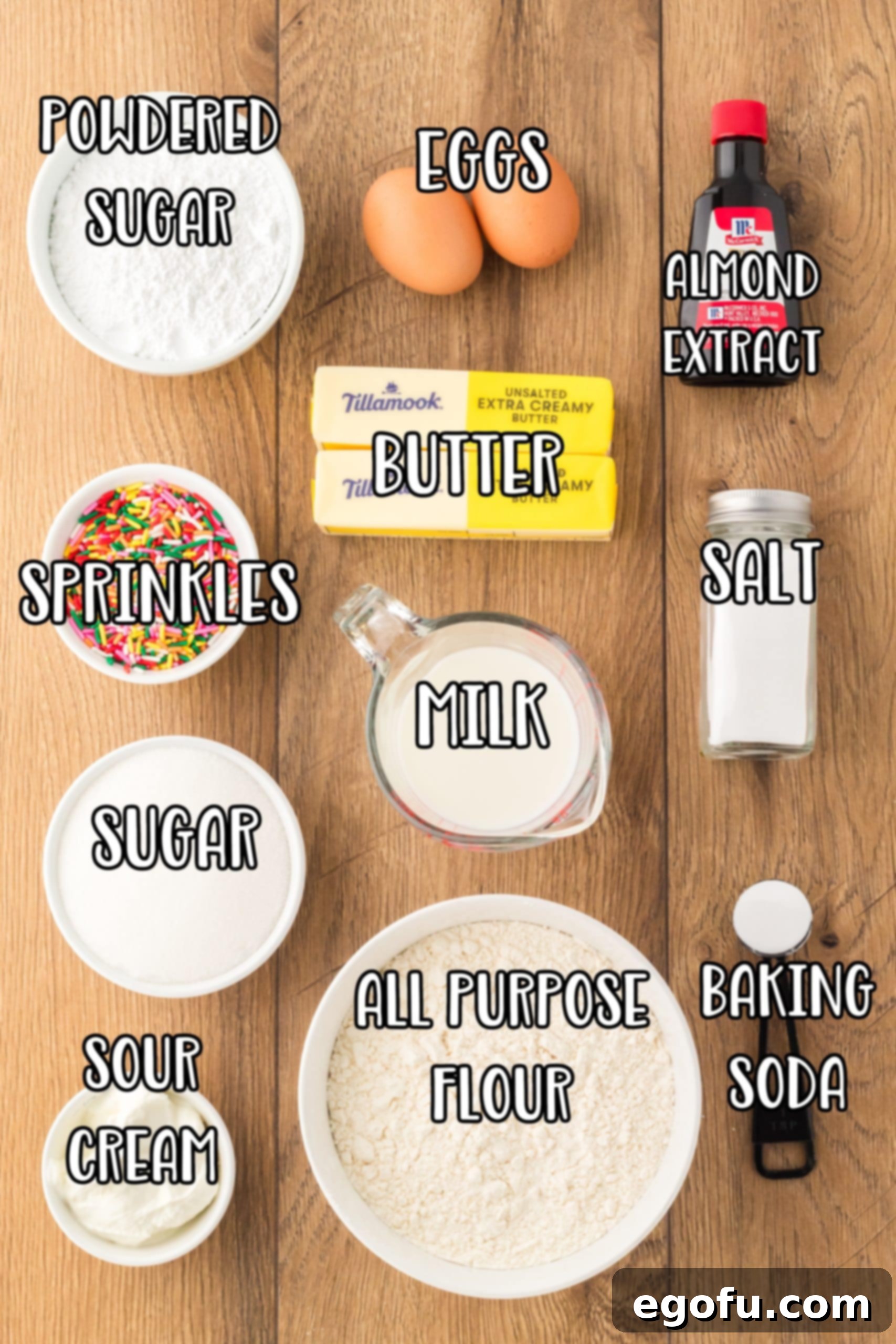 A vibrant flat lay of all the essential ingredients for White Texas Sheet Cake: almond extract, milk, all-purpose flour, eggs, powdered sugar, granulated sugar, butter, baking soda, salt, and water, neatly arranged on a countertop.