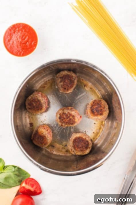 Several meatballs actively searing and browning in the hot oil inside an Instant Pot, developing a delicious crust.