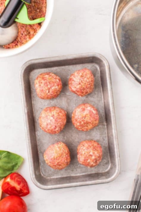 Six large, perfectly shaped meatballs resting on a sheet pan, ready for searing.