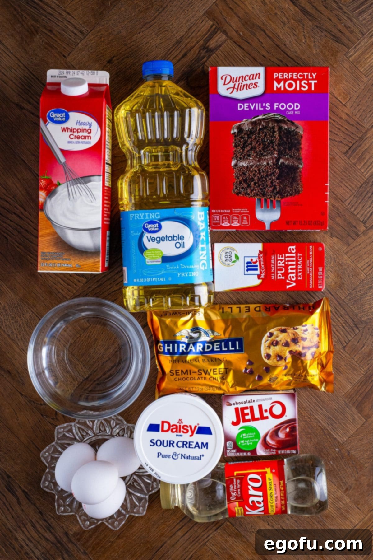 Velvet Chocolate Pudding Bundt 4 An array of ingredients for Chocolate Pudding Bundt Cake including devil's food cake mix, vegetable oil, eggs, sour cream, heavy cream, pudding mix, vanilla extract, light corn syrup, and chocolate chips.