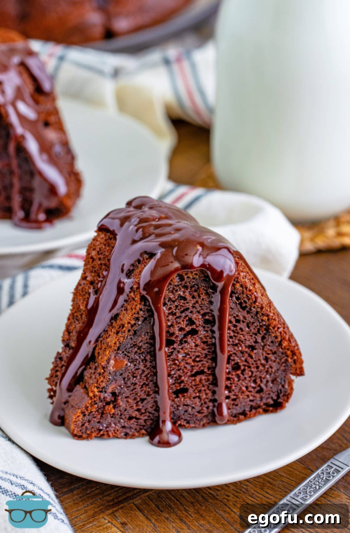 Velvet Chocolate Pudding Bundt 9 A large piece of Chocolate Pudding Bundt Cake with generous chocolate sauce on top, served on a white dessert plate.