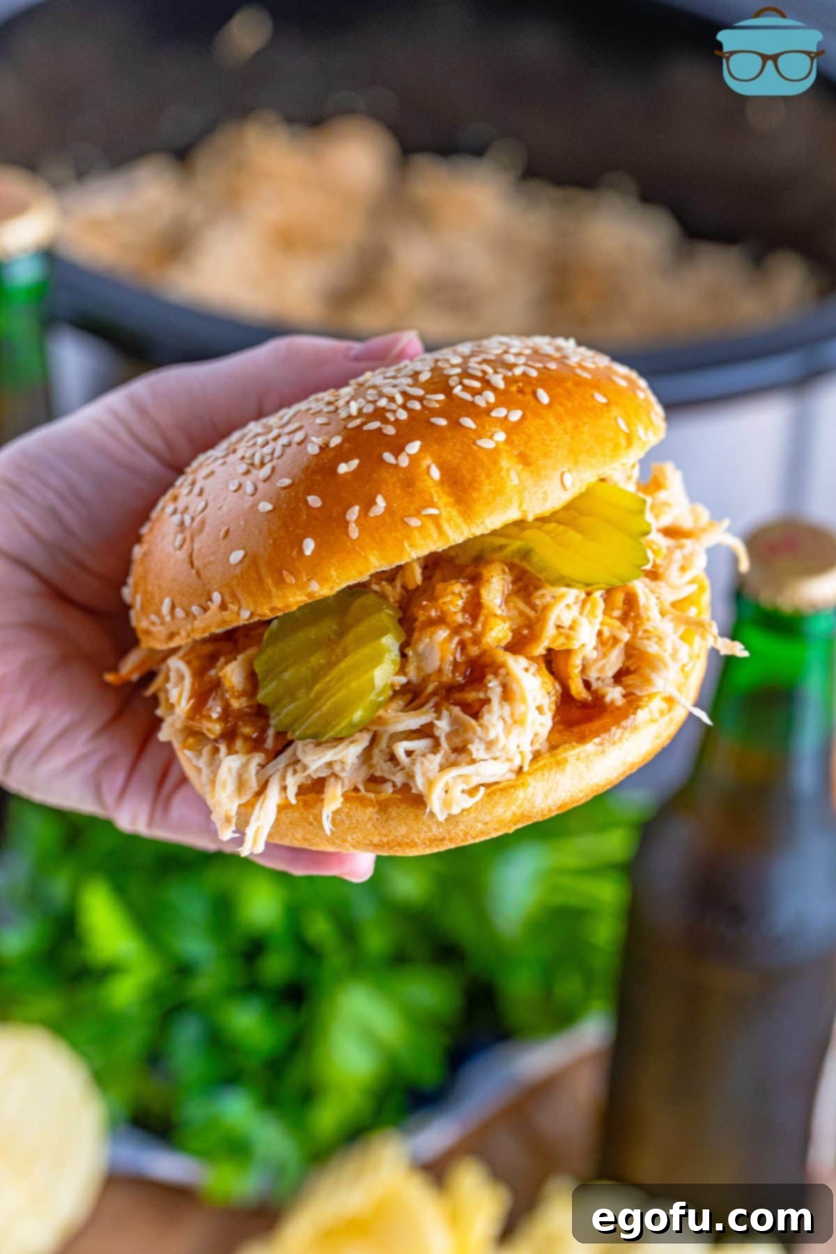 A hand holding some Shredded Nashville Hot Chicken on a sandwich bun.