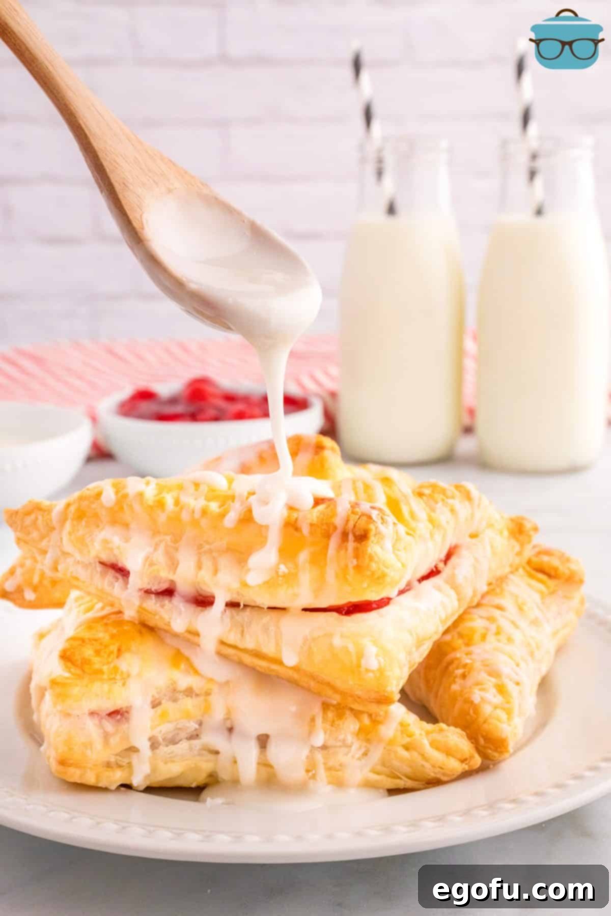 Glaze being poured generously over a stack of golden-brown Cherry Turnovers, creating a tempting dessert presentation.
