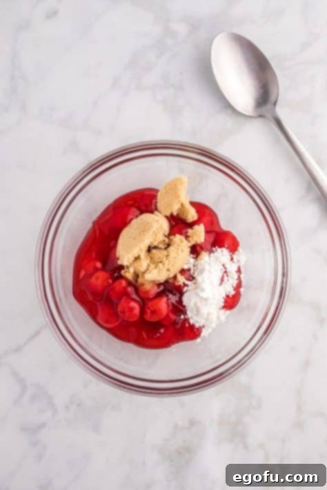 A bowl with cherry pie filling, brown sugar, cornstarch, and almond extract, stirred together.