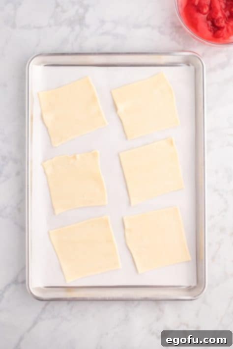 Cut squares of puff pastry arranged on a parchment-lined baking sheet.