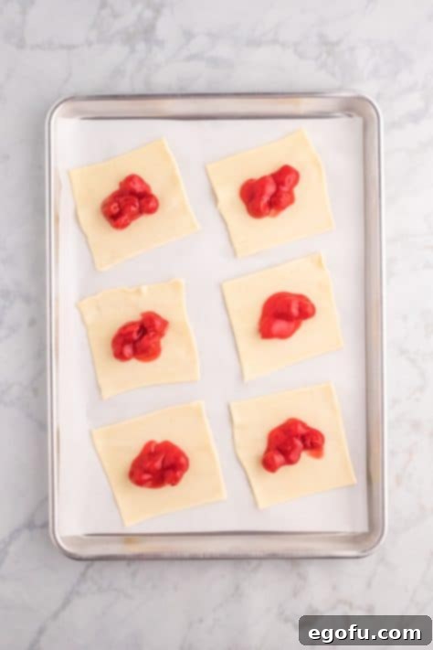 A tablespoon of cherry filling placed in the center of a puff pastry square.