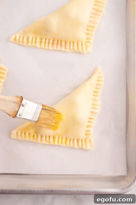 A pastry brush applying egg wash to the top of a cherry turnover.
