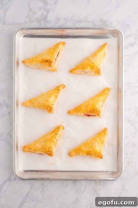 Golden-brown and puffed cherry turnovers fresh out of the oven on a baking sheet.