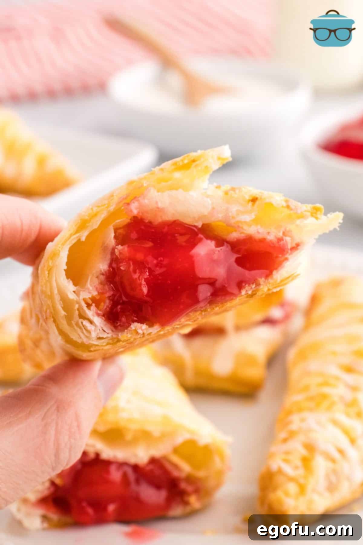 A close-up of a hand gently breaking open a freshly baked Cherry Turnover, revealing its warm, luscious cherry filling and flaky layers.