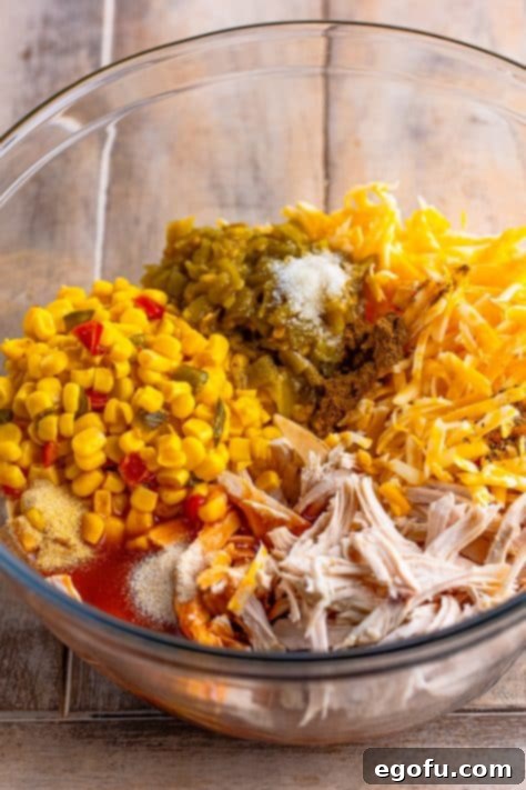 Cheesy Chicken Enchilada Fiesta 11 A large mixing bowl containing shredded chicken, southwestern corn, green chiles, shredded cheese, enchilada sauce, and various spices, all well combined.