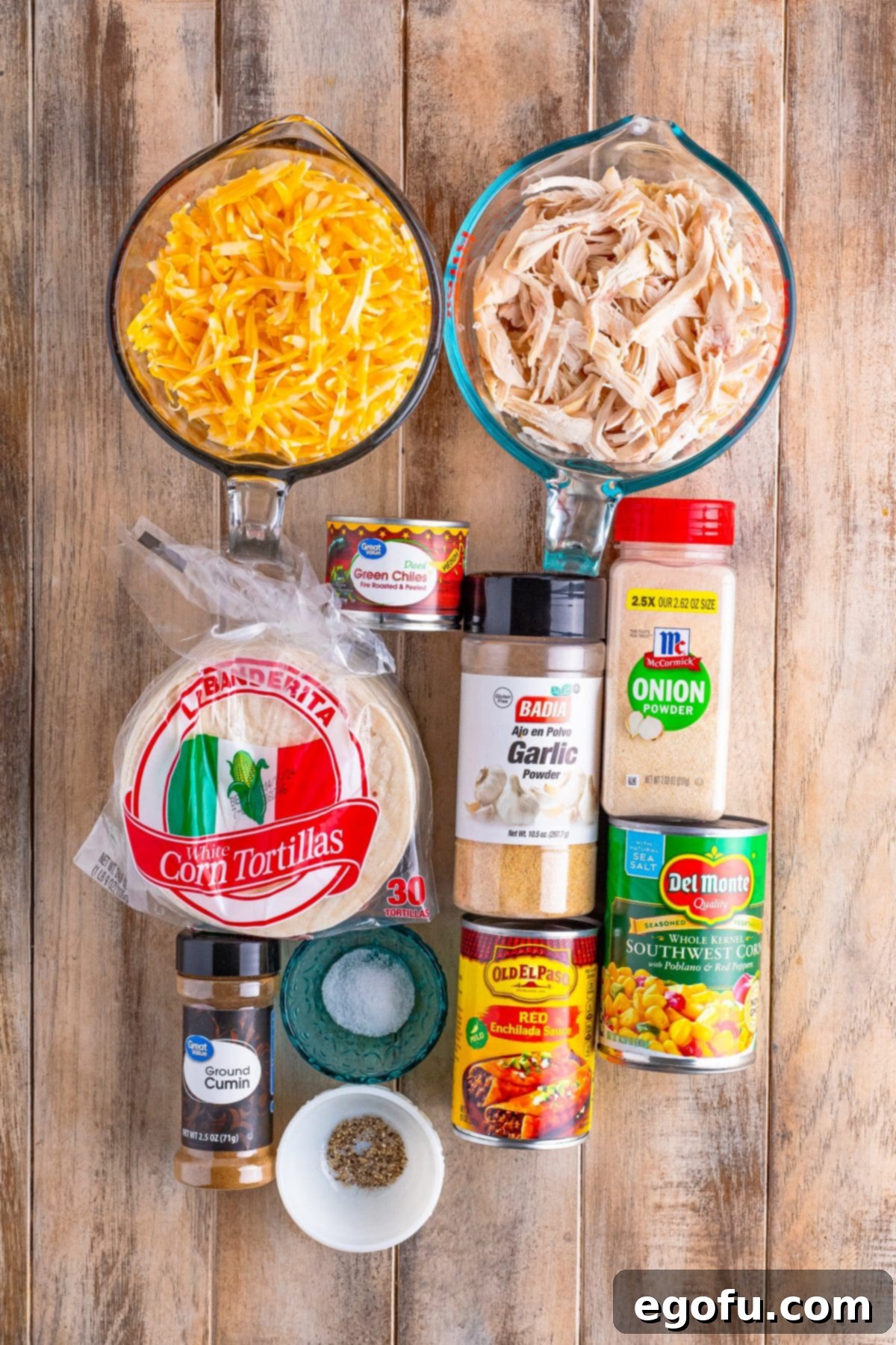 Cheesy Chicken Enchilada Fiesta 4 A visual display of all the key ingredients: shredded cooked chicken, southwestern corn, green chiles, shredded Colby Jack cheese, enchilada sauce, various spices, and corn tortillas.