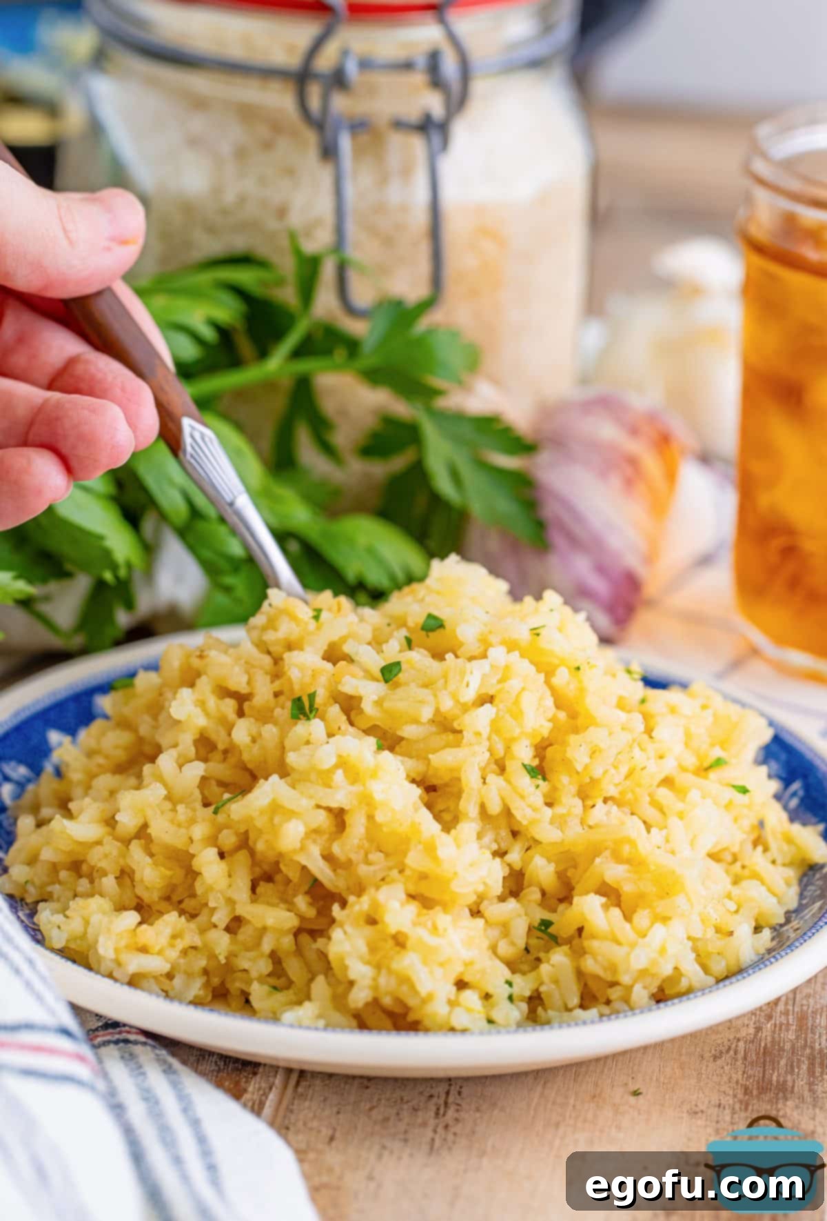 A hand holding a fork takes a bite of the fluffy, aromatic Garlic Butter Rice from a serving dish, ready to savor its rich flavor.