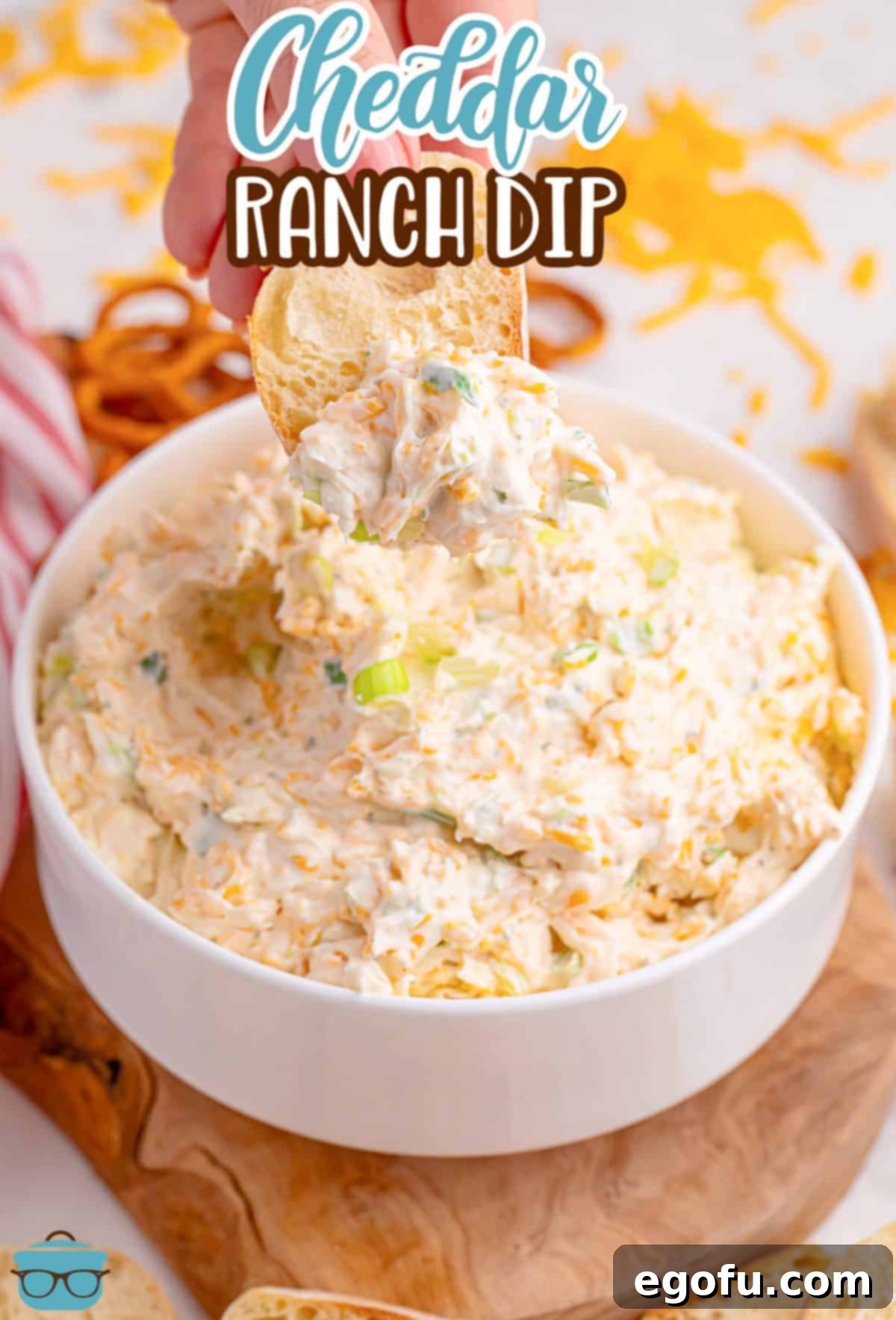 A piece of bread being dipped into some creamy Cheddar Ranch Dip, showing its thick texture.
