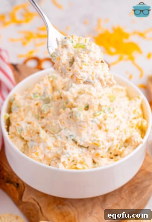 A fork holding a scoop of creamy Cheddar Ranch Dip, garnished with green onions.