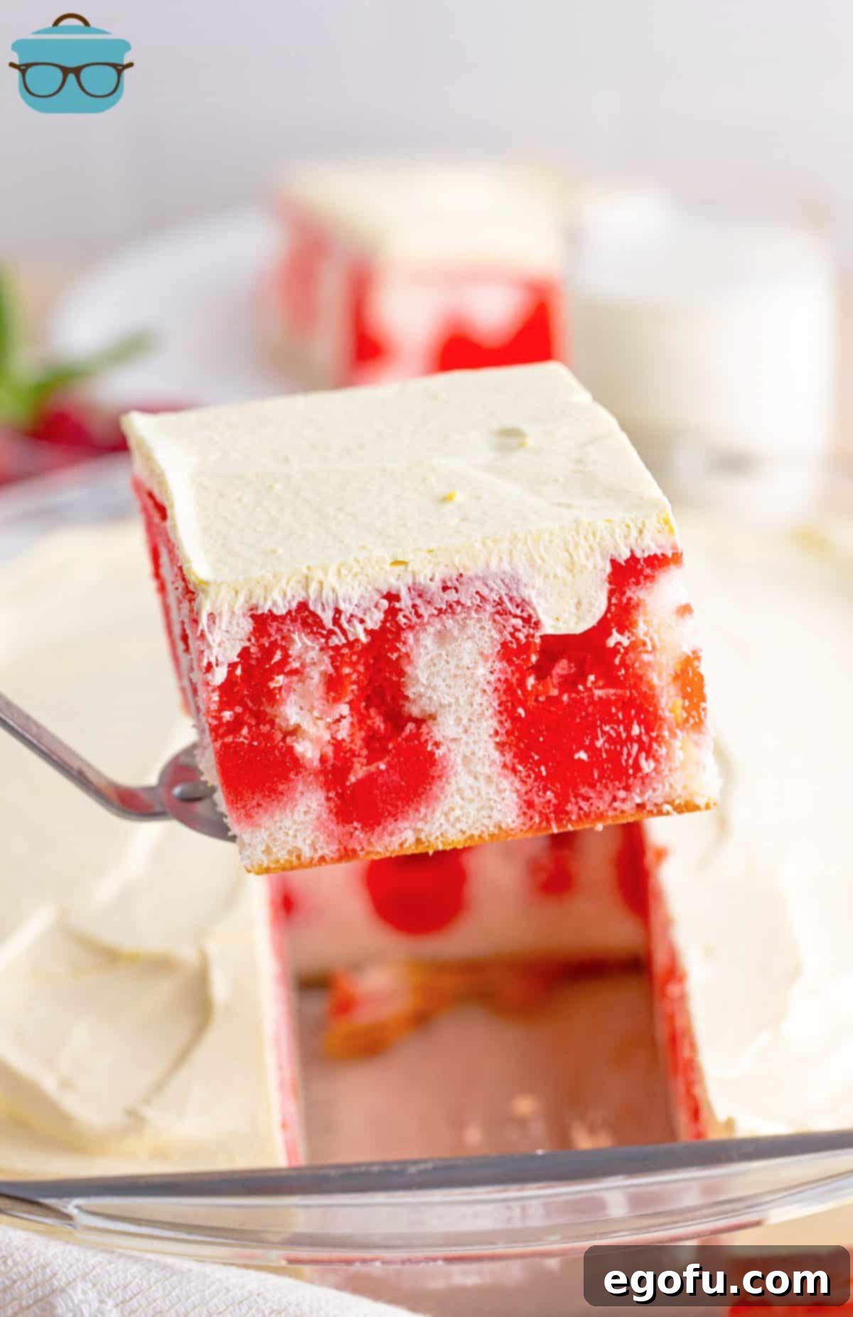 A serving utensil lifting a slice of Raspberry Poke Cake, revealing its beautiful layers.