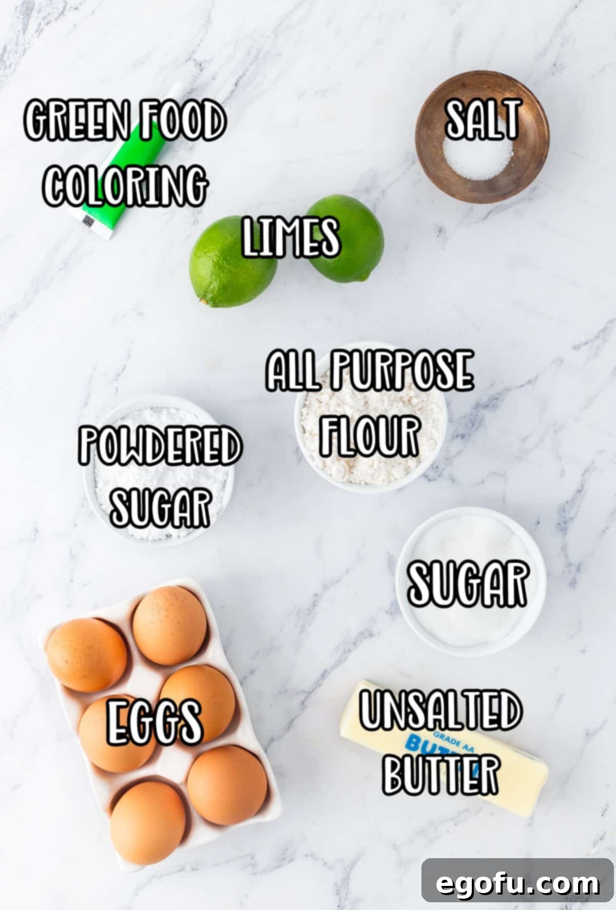 A vibrant flat lay of all the essential ingredients for making Lime Bars: green food coloring, fresh eggs, creamy butter, all-purpose flour, fine powdered sugar, bright limes, granulated sugar, and unsalted butter.