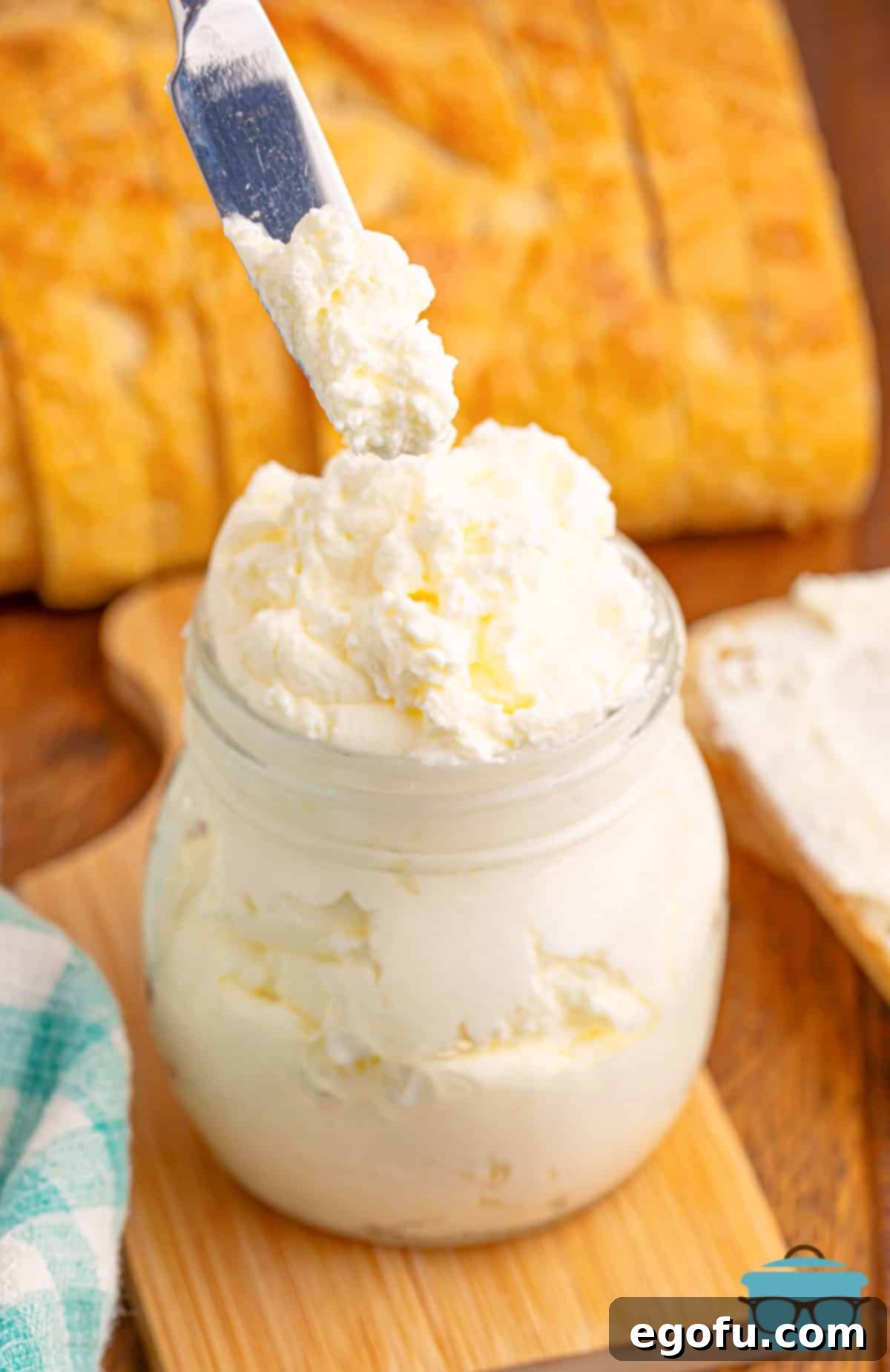 A butter knife gracefully scooping a generous portion of fluffy homemade whipped butter from a glass jar.