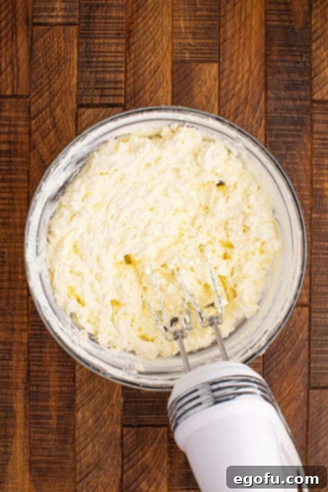 Heavy cream and kosher salt being mixed together in a bowl with an electric mixer, showing the separation into butter.