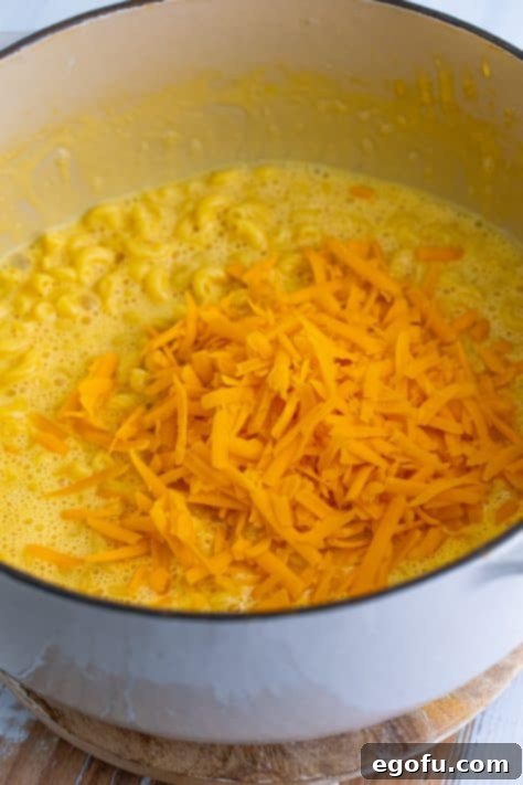Shredded sharp cheddar cheese being added to the creamy macaroni in the pot.