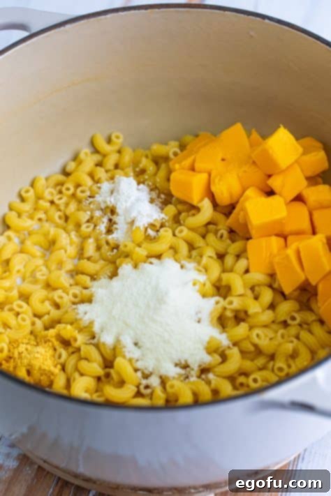 Cooked macaroni in a pot with whole milk, powdered milk, cornstarch, dry ground mustard, and cubed Velveeta cheese.