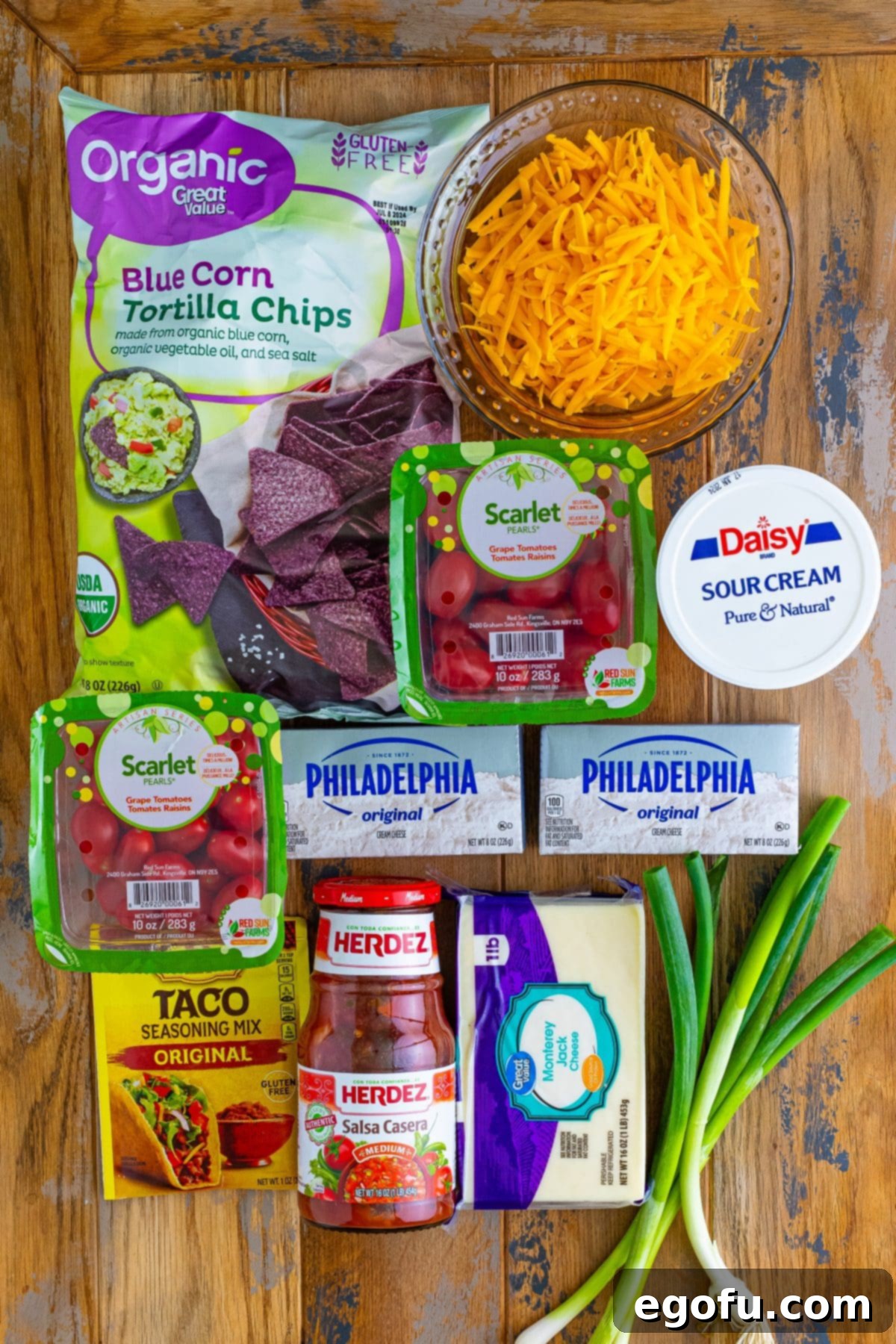 Stars and Stripes Celebration Dip 4 A vibrant flat lay of all ingredients for the 4th of July Flag Dip: blue tortilla chips, sour cream, Monterey Jack cheese, cheddar cheese, grape tomatoes, cream cheese, green onions, taco seasoning, and salsa.
