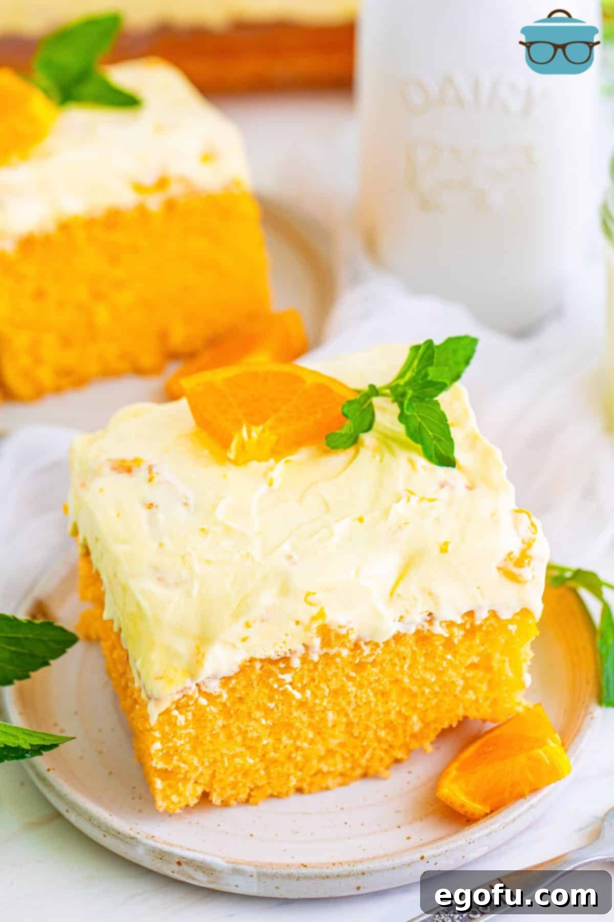 A slice of Orange Poke Cake on a small white dessert plate, showcasing its layers and creamy topping.