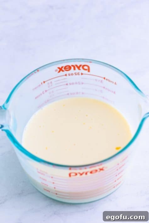 Sweetened condensed milk and mandarin orange juice in a measuring cup.