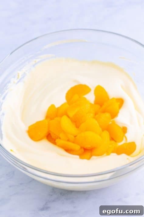 Oranges being added to a sweet creamy mixture in a mixing bowl.
