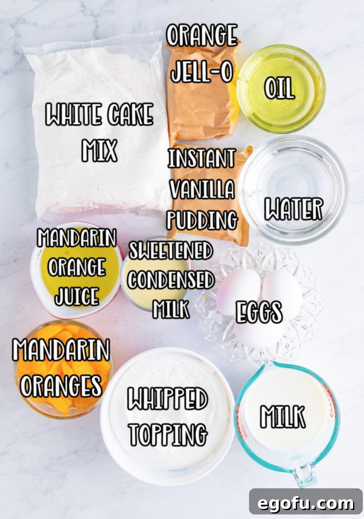 A flat lay photograph displaying all the ingredients for Orange Poke Cake: white cake mix, egg whites, oil, water, orange Jell-O, mandarin oranges with juice, sweetened condensed milk, French vanilla pudding mix, whole milk, and whipped topping.