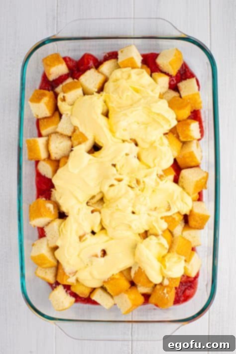 A pudding mixture spread over pound cake and strawberry pie filling in a dish.