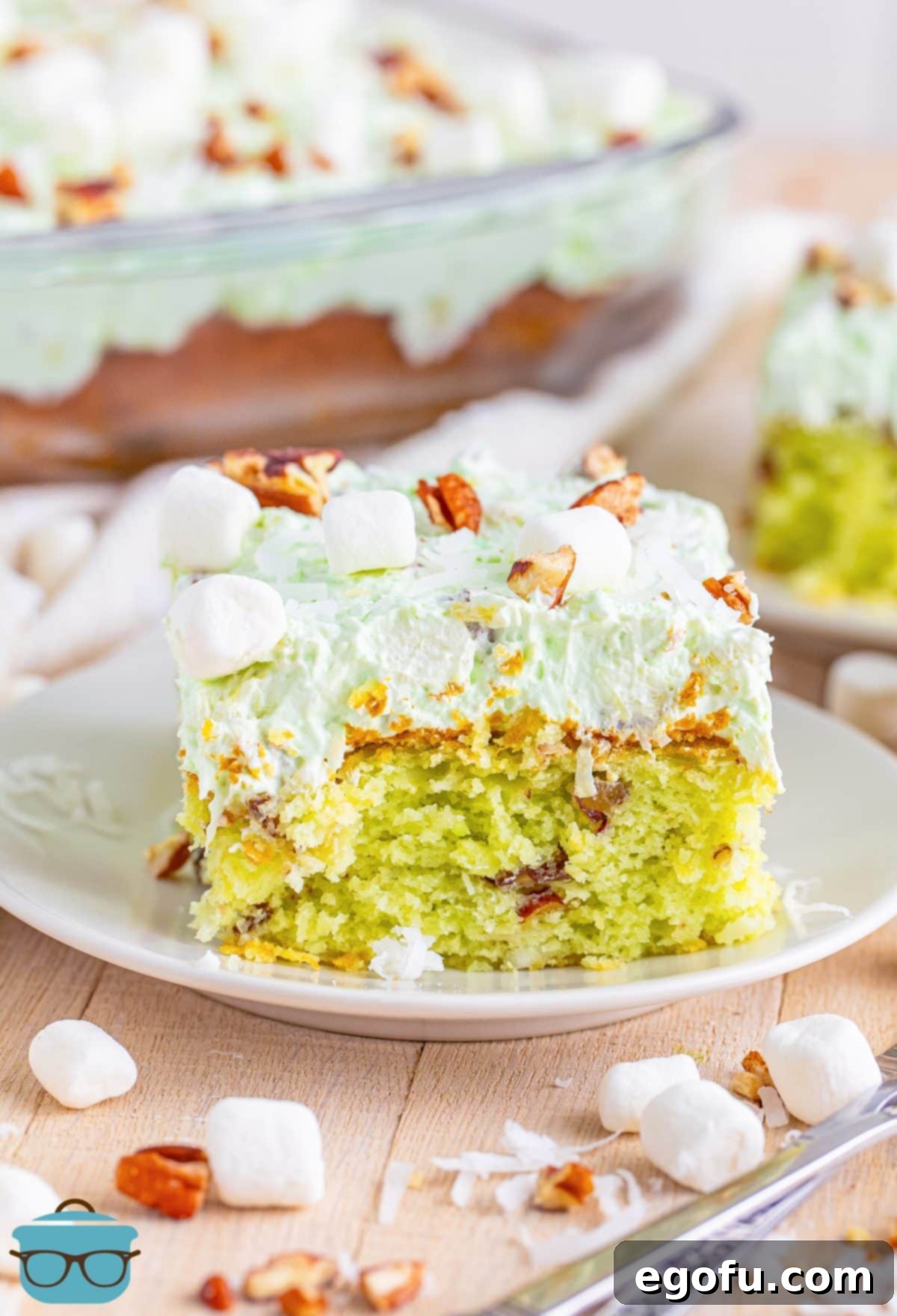 A beautifully sliced piece of Watergate Cake on a white dessert plate, showcasing its vibrant green color and fluffy topping.
