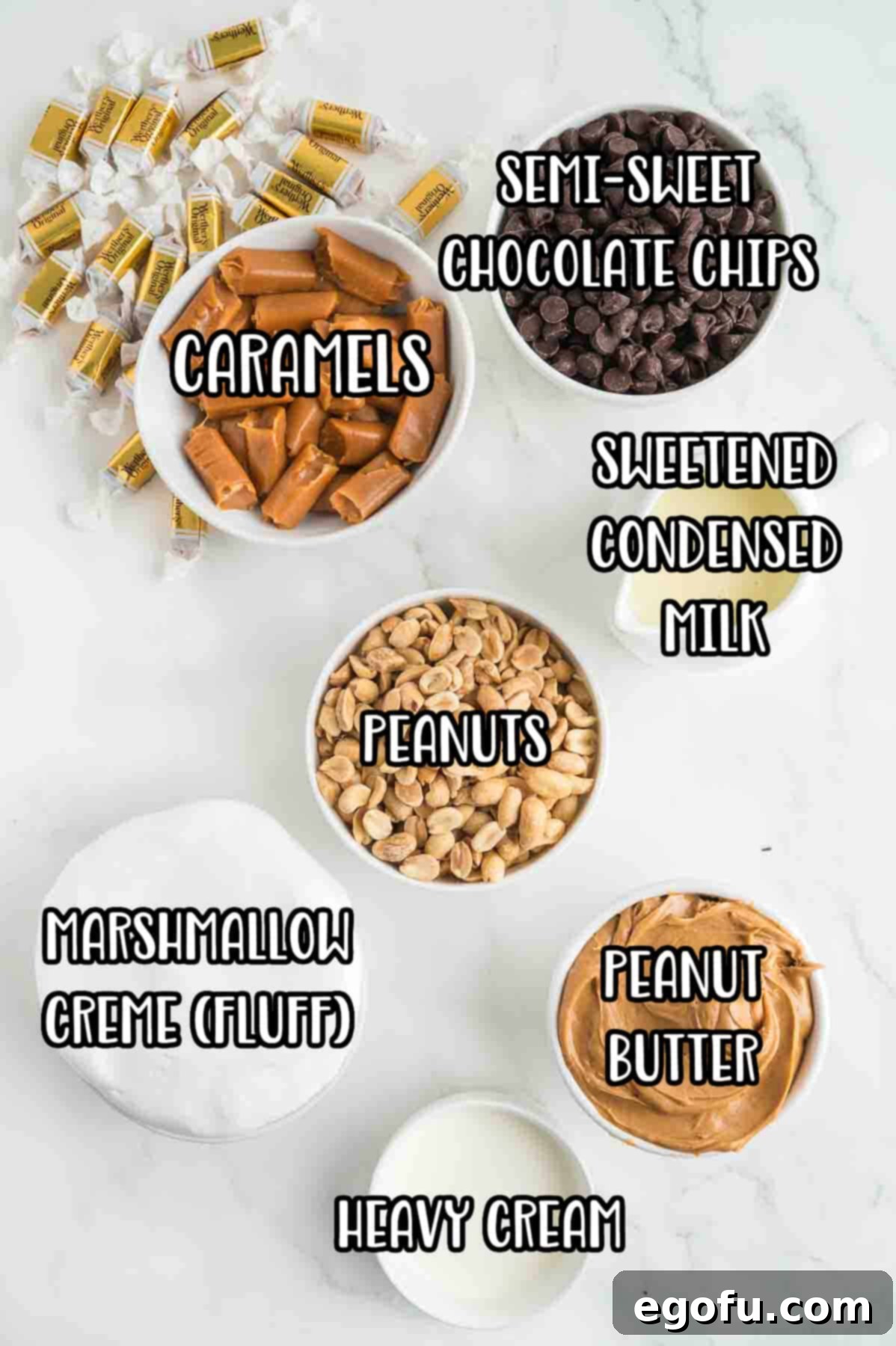 A flat lay of all the essential ingredients: semi-sweet chocolate chips, soft caramels, heavy cream, sweetened condensed milk, salted peanuts, creamy peanut butter, and marshmallow creme.