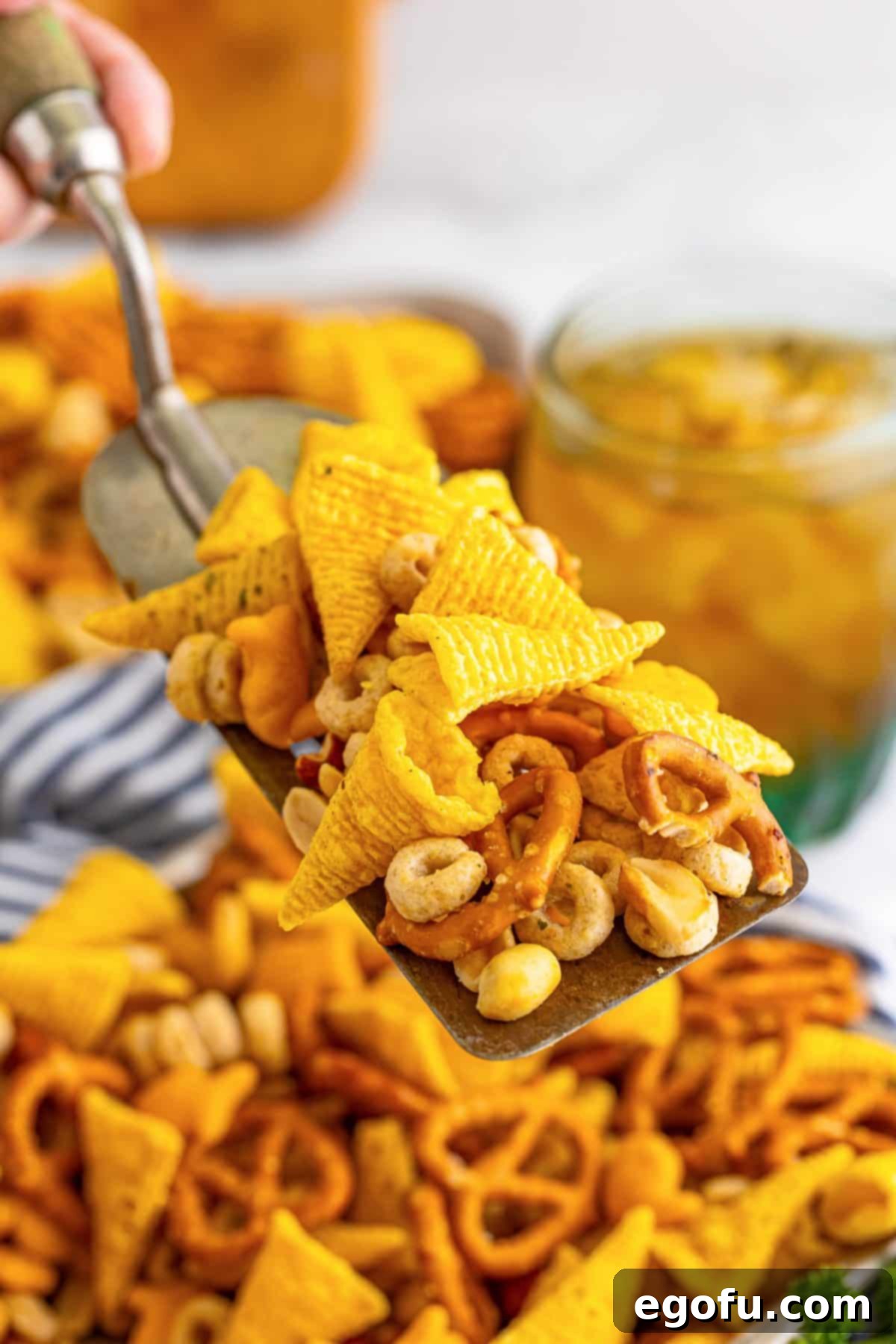 A scoop of Ranch Bugle Snack Mix being dumped into a tray of it. 