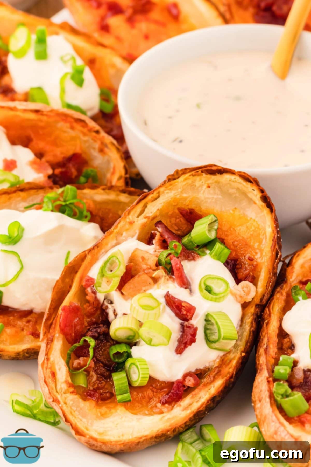 A few Air Fryer Potato Skins arranged around a bowl of sour cream, garnished with green onions and ready for serving.