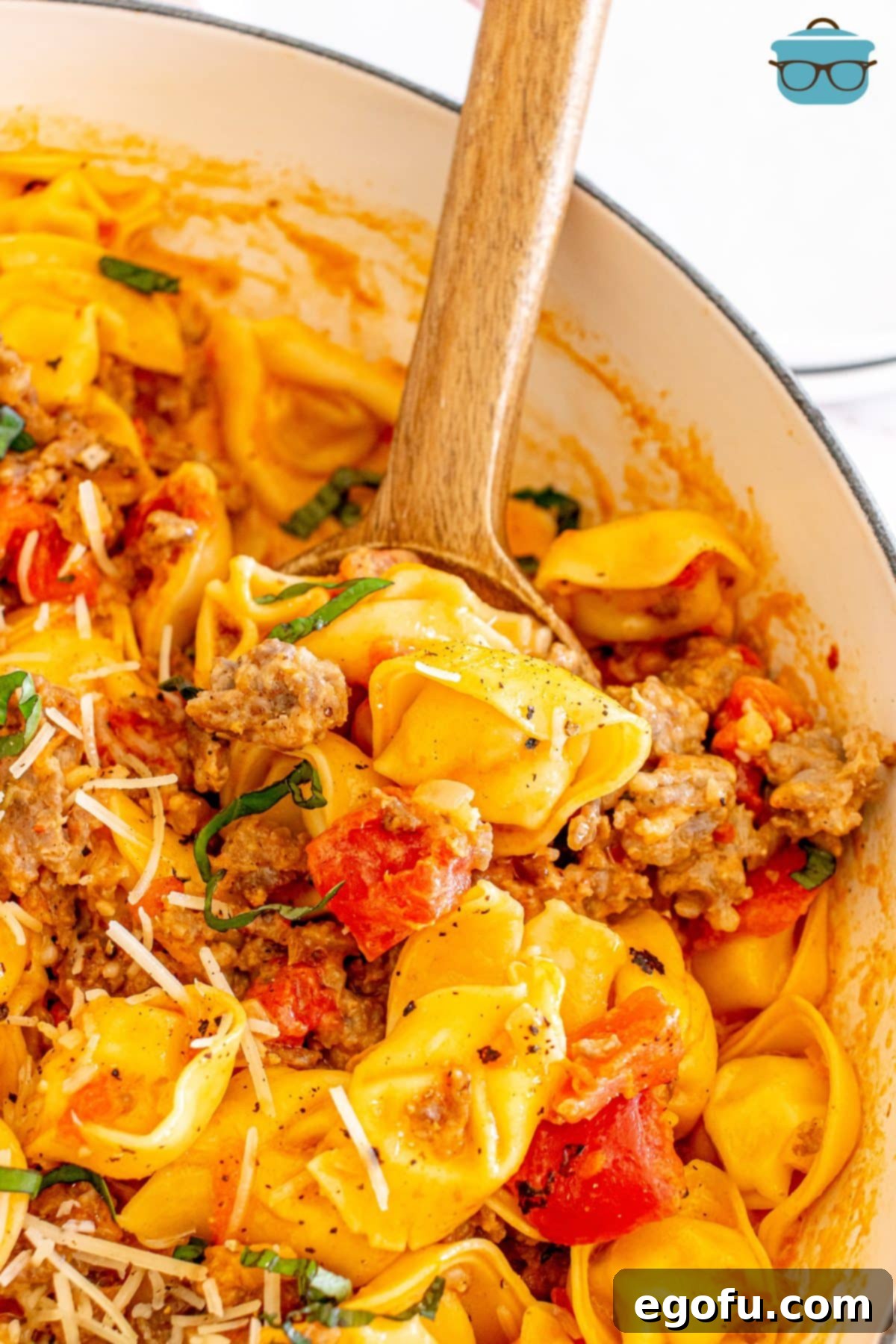 Creamy One-Pot Sausage Tortellini 2 A wooden spoon in a pot of creamy One Pot Sausage and Tortellini, garnished with fresh basil.