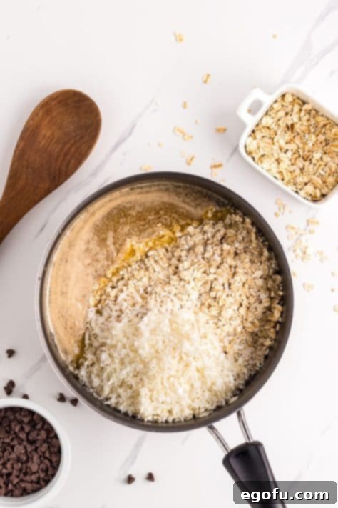 Oats and coconut on top of butter, brown sugar, vanilla, cinnamon, and salt in a saucepan, ready to be mixed into the base.