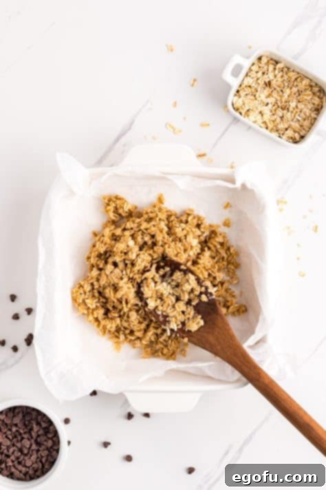 The initial oat mixture being pressed firmly into the bottom of a baking dish, forming the base layer.